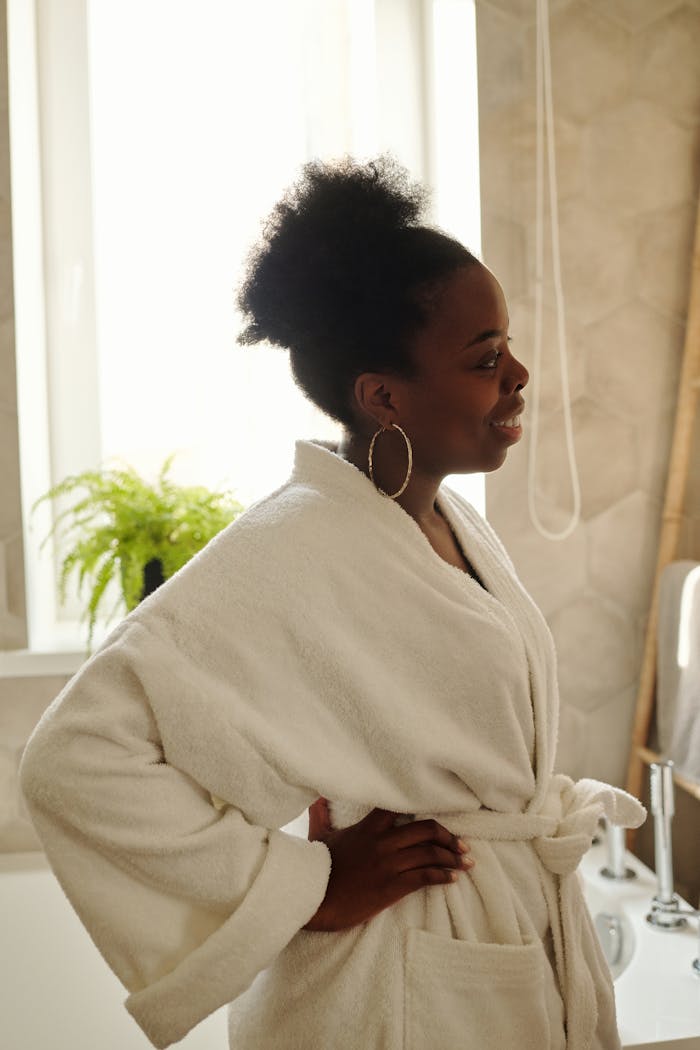 A woman in a bathrobe smiling in a bathroom, enjoying a leisurely morning.